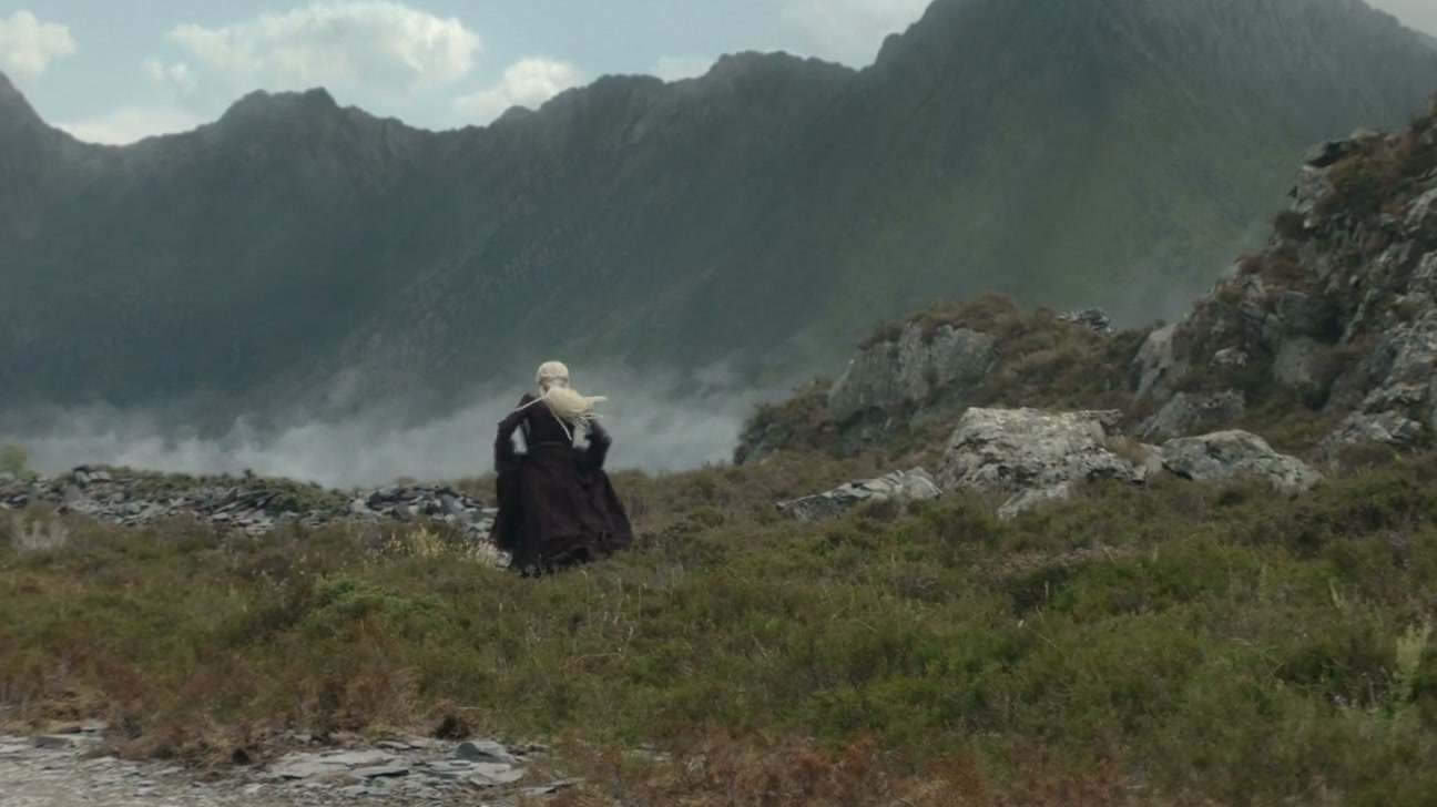 A lone figure crossing a moor towards a mountain wall in mist