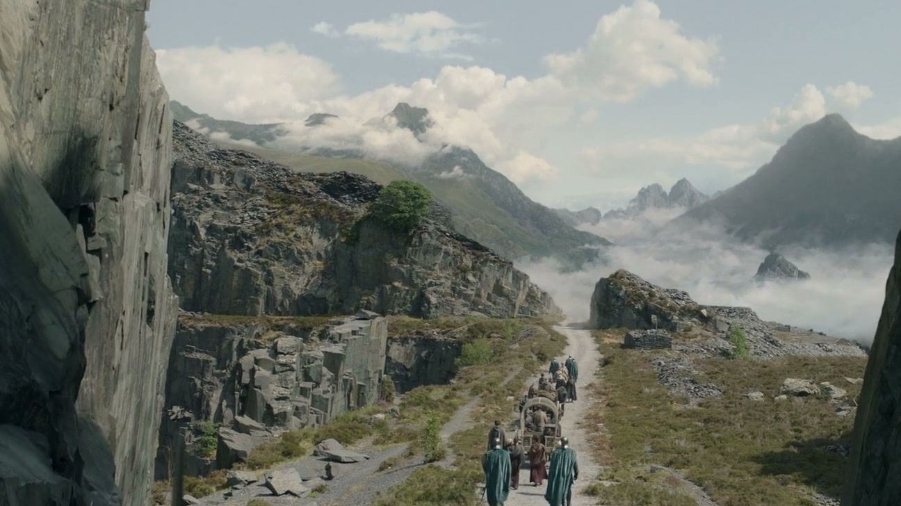 A column of travellers on a mountain road through a gorge, mist and peaks beyond